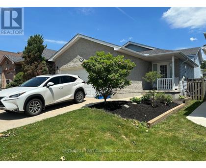A white car is parked in front of a house with a tree and a flower bed.