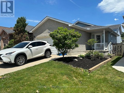 A white car is parked in front of a house with a tree and a flower bed.