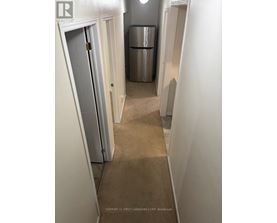 A hallway with a door on the left and a fridge in the middle.