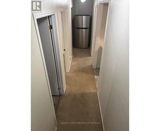 A hallway with a door on the left and a fridge in the middle.