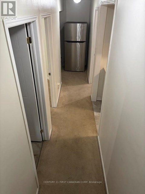A hallway with a door on the left and a fridge in the middle.