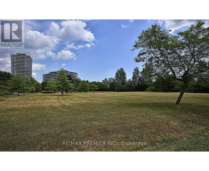 A grassy field with trees and buildings in the background.