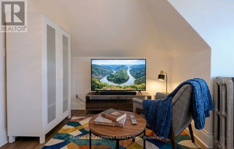 A living room with a television on a stand and a chair with a blue blanket on it.