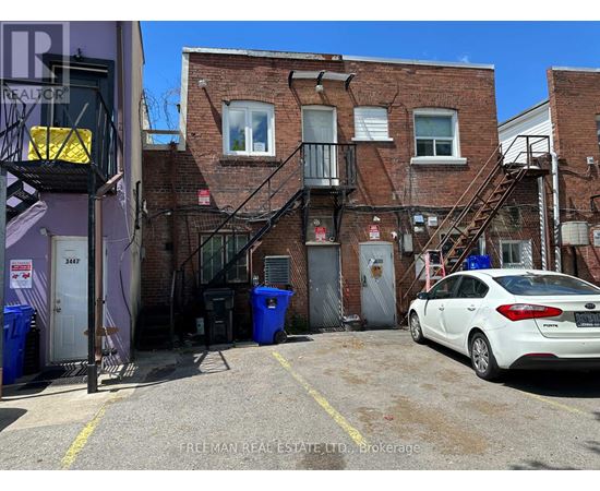 A white car is parked in a parking lot in front of a brick building.