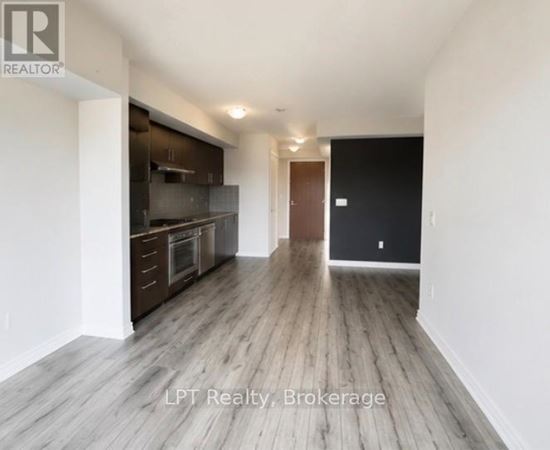 A spacious room with wooden flooring and a kitchen area in the background.