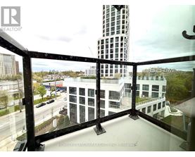A balcony with a glass railing overlooks a city street and buildings.
