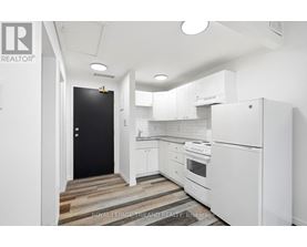 A white kitchen with a black door and wooden flooring.