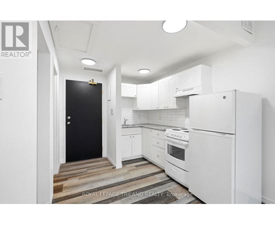 A white kitchen with a black door and wooden flooring.
