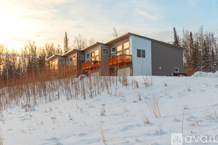 A modern house with a balcony is surrounded by snow and trees.
