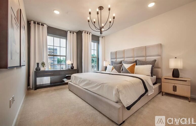 A bedroom with a large bed, a chandelier, and a window with curtains.