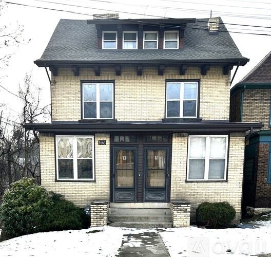 A house with a black door and windows is surrounded by snow.