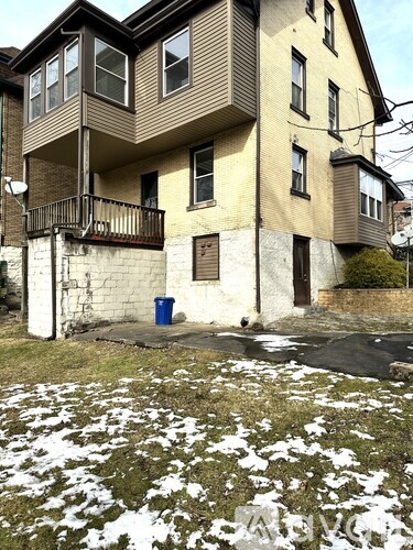 A two-story apartment building with a balcony and a blue trash can in front.