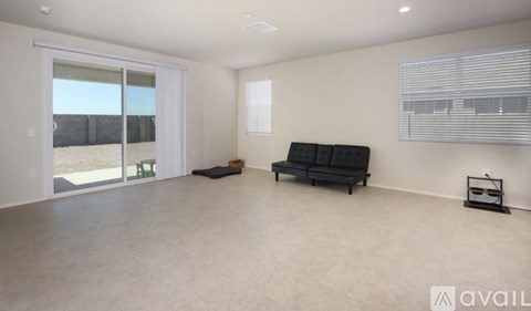 A spacious living room with a black sofa and a sliding glass door leading to a backyard.