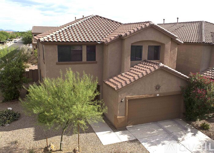 A house with a brown roof and tan walls has a garage and a tree in front of it.
