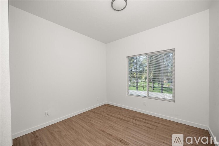 A room with wooden flooring and a window showing a view of trees.