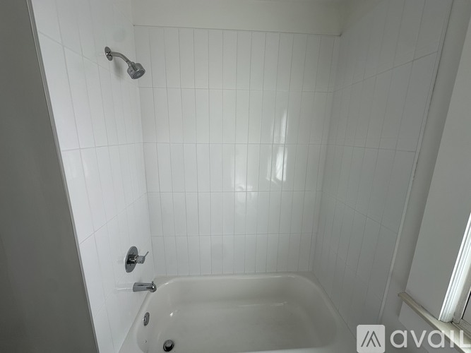 A white tiled bathroom with a white bathtub and shower head.