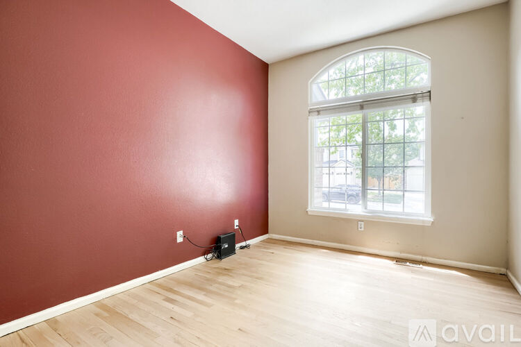 A room with a red wall and a window with a view of trees and a building outside.