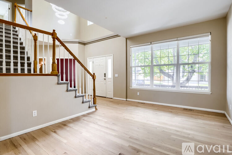 A spacious room with wooden floors and a staircase with red and white railings.