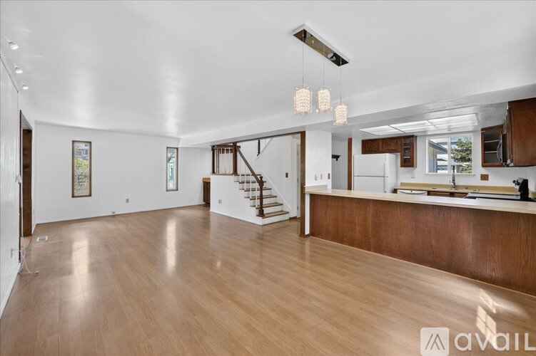 A spacious living room with wooden floors and a staircase leading to the upper level.