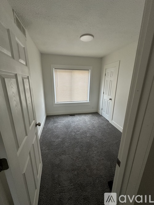 A hallway with a carpeted floor and a window with blinds.