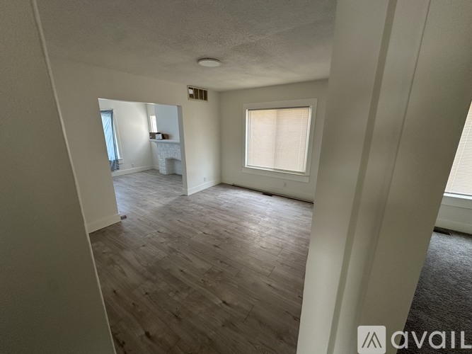 A spacious room with wooden flooring and a window with blinds.