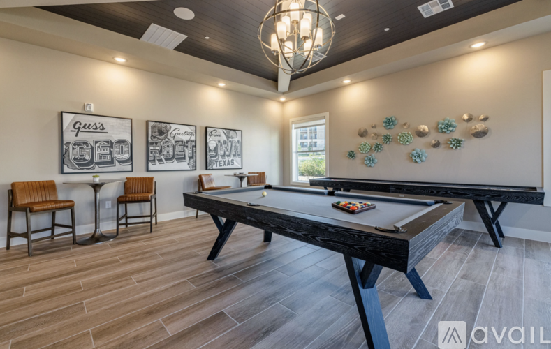 A pool table is in the middle of a room with a light brown floor and a chandelier hanging from the ceiling.