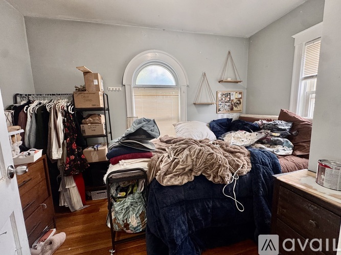 A messy bedroom with a bed in the center and clothes hanging on a rack.