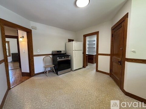A kitchen area with a fridge, stove, and a chair.