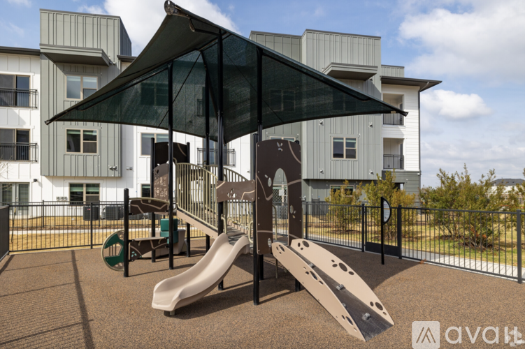 A playground with a slide and a canopy is in front of a building.