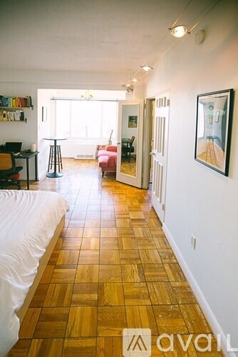 A long hallway with a white bed on the left and a red couch on the right.