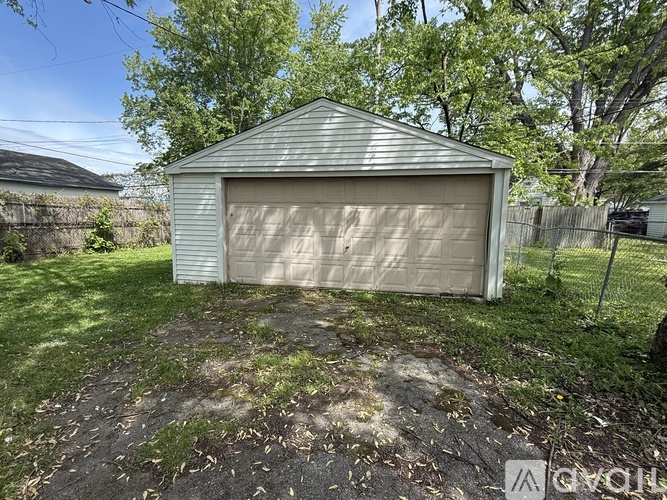 A detached garage with a white door is surrounded by a grassy area and trees.