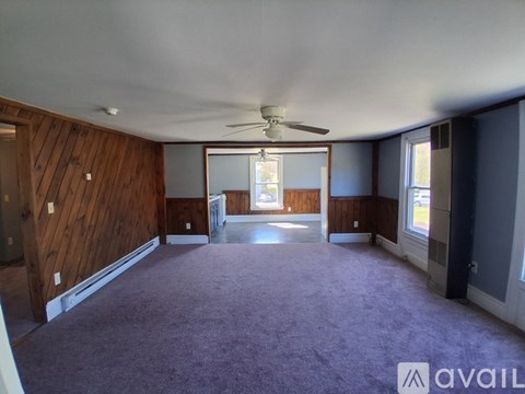 A spacious room with a ceiling fan and purple carpeting.