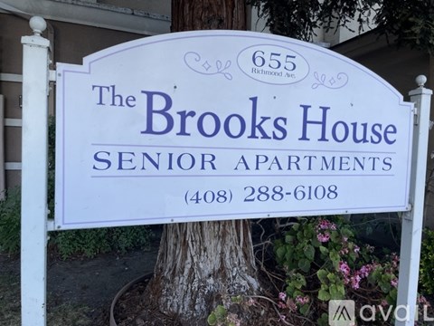 A sign for The Brooks House Senior Apartments is displayed in front of a tree.