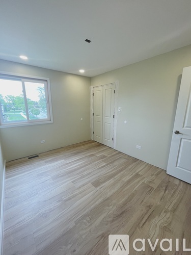 A room with wooden flooring and a window showing a view of a green area outside.