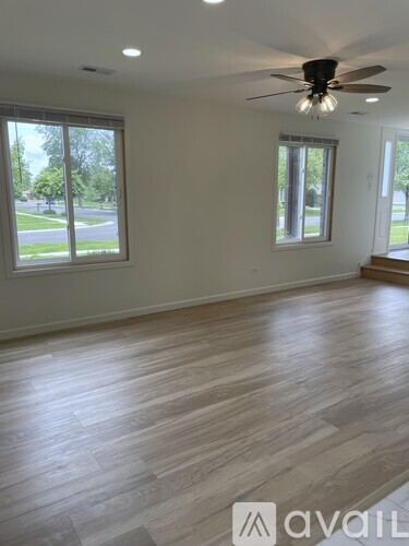 A room with a ceiling fan and lighting fixture, and a window with a view of a green lawn and trees.