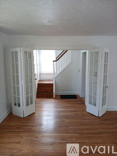 A room with wooden floors and white walls with a staircase in the background.