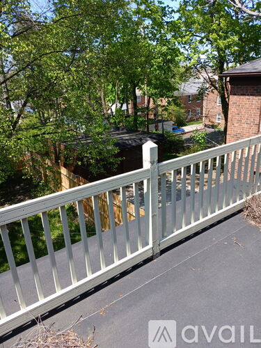A white railing on a balcony with trees and a house in the background.