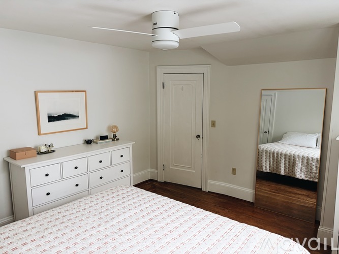 A bedroom with a white ceiling fan and a bed with a white and red patterned comforter.