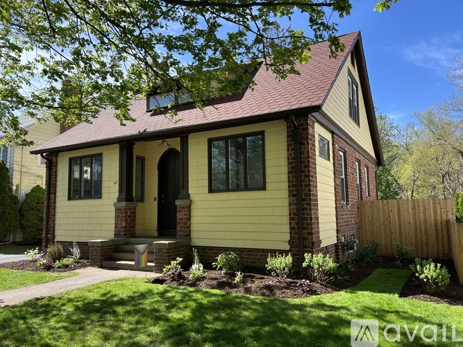 A house with a red roof and a yellow exterior is surrounded by a wooden fence and greenery.
