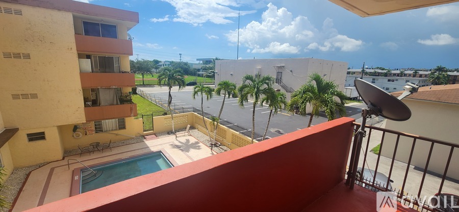 A balcony with a satellite dish overlooks a pool and apartment buildings.