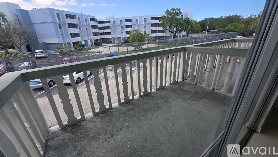 A balcony with a railing overlooks a parking lot and buildings.