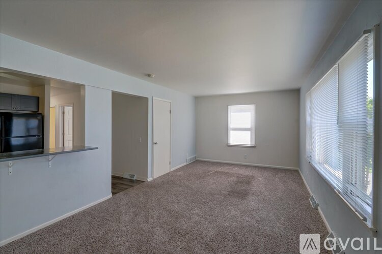 A spacious room with a carpeted floor and a window with blinds.