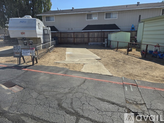 A cracked driveway leads to a house with a trailer and a shed.