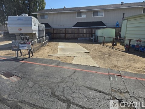 A cracked driveway leads to a house with a trailer and a shed.
