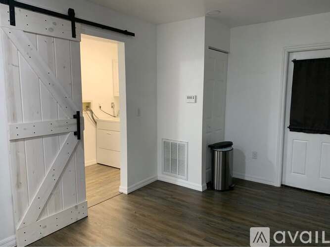 A white wooden door is open to a room with a trash can.