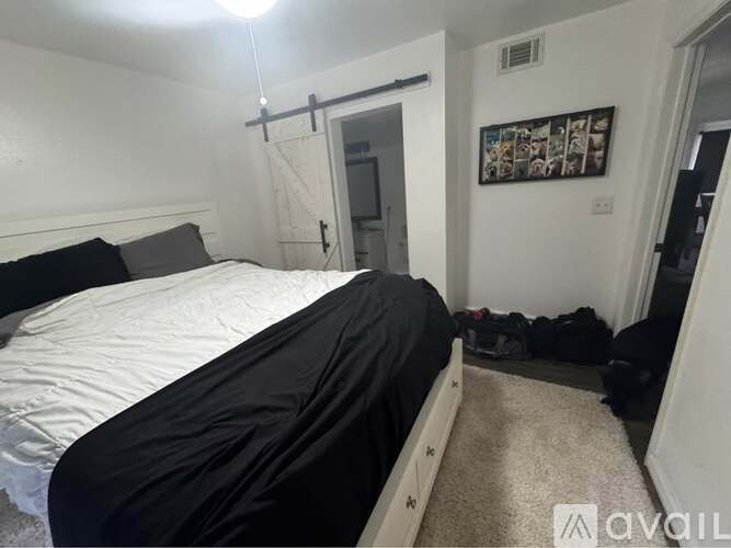 A bedroom with a bed covered in a black sheet and a carpeted floor.