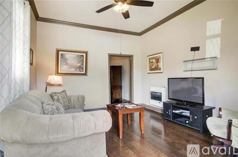 A living room with a grey couch, a wooden coffee table, a television, and a ceiling fan.