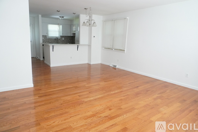A room with wooden flooring and a kitchen area in the background.