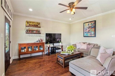 A living room with a couch, a coffee table, a ceiling fan, and a wall with a painting and a shelf with bottles.