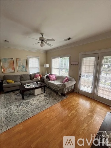 A living room with a grey couch, a coffee table, a bed with a pink blanket, and a ceiling fan.